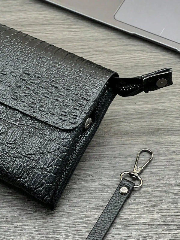 Schwarze Krokodilmuster-Clutchtasche mit Lederriemen auf grauem Holzuntergrund.