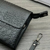 A black crocodile pattern clutch bag with a leather strap resting on a gray wooden surface.