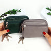 A hand holds a dark green and gray PU leather mini wallet with a keychain against a white background.