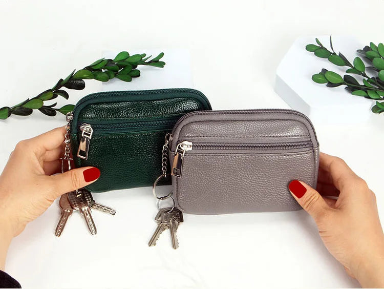 A hand holds a dark green and gray PU leather mini wallet with a keychain against a white background.