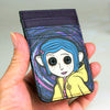 A hand holds a purple and blue credit card holder featuring an illustration of an alien character.