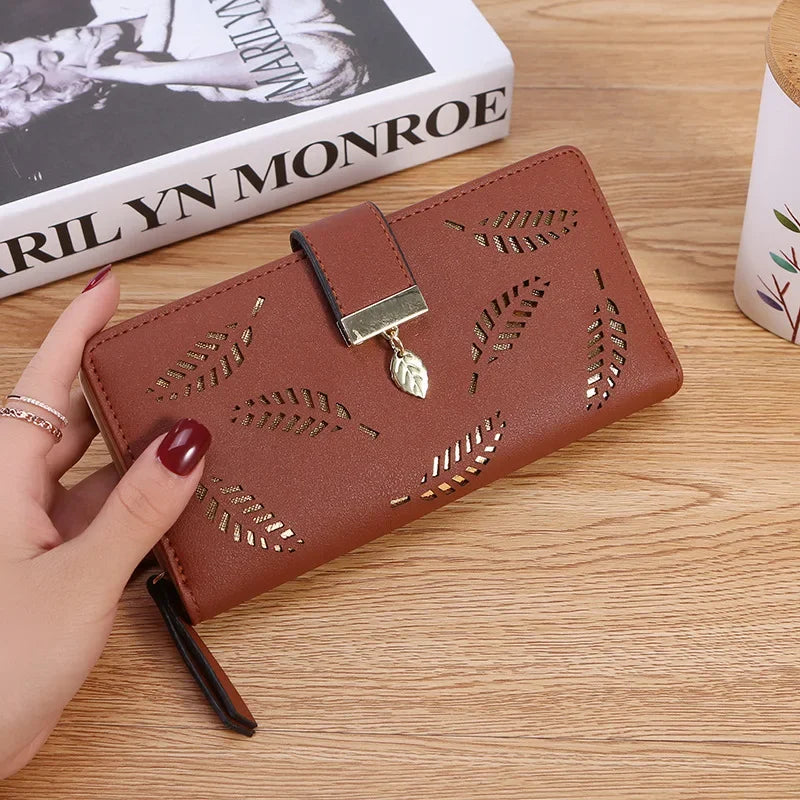 Cartera de cuero PU marrón con detalles dorados, sostenida por una mano sobre una superficie de madera.