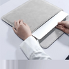 A hand is placing a white laptop into a gray padded sleeve, demonstrating a hidden magnetic bracket feature.