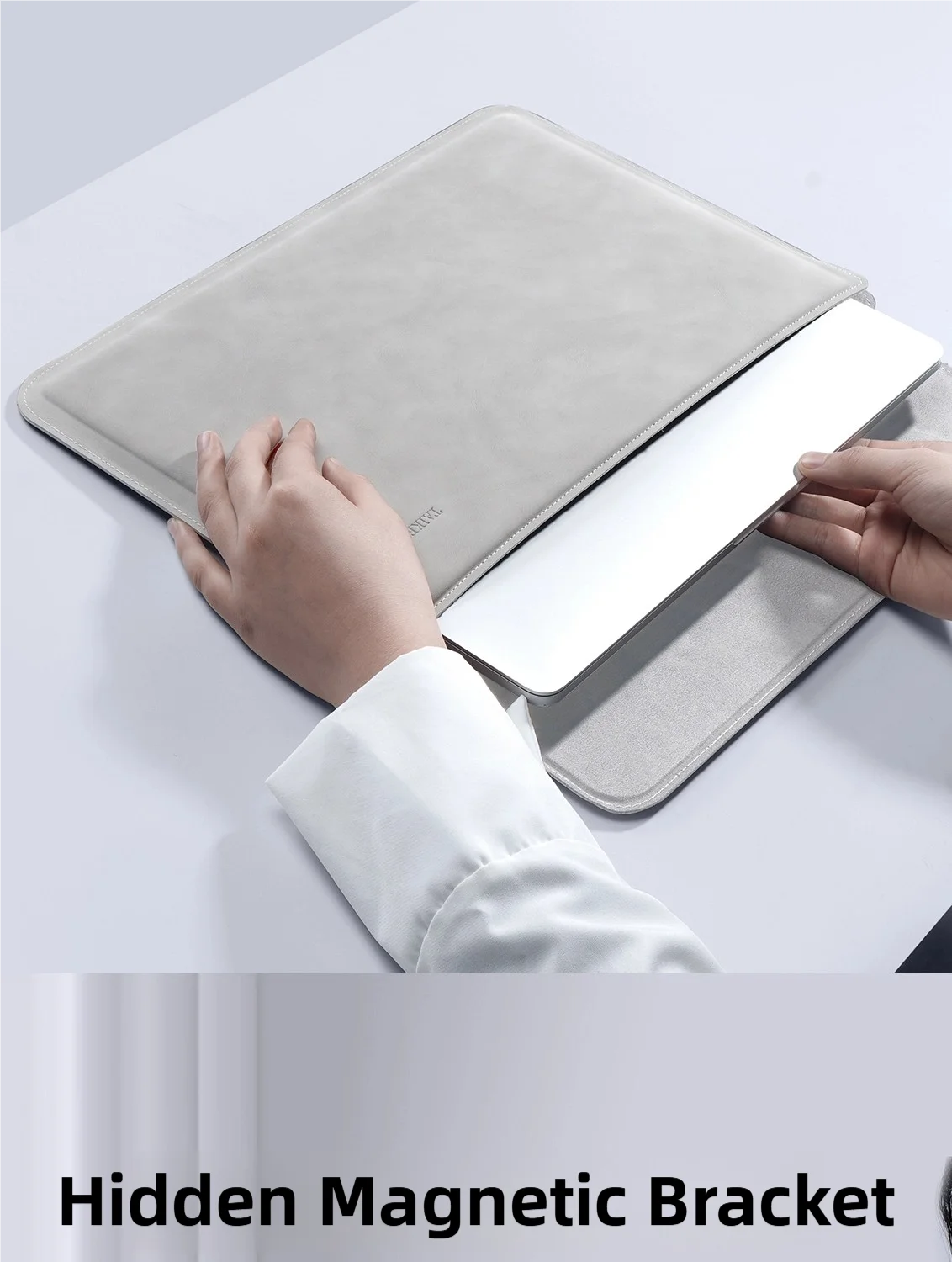 A hand is placing a white laptop into a gray padded sleeve, demonstrating a hidden magnetic bracket feature.