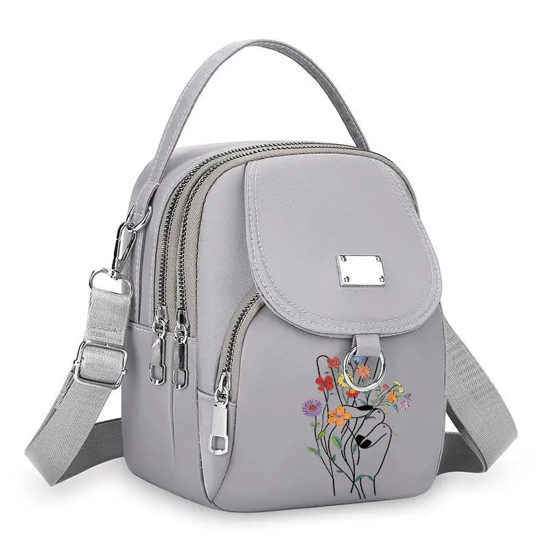 Sac bandoulière floral gris clair et durable avec fermeture éclair et sangle réglable.