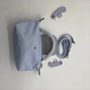 A light blue waterproof nylon crossbody bag with a detachable mini pouch and strap accessories hanging on a white wall.