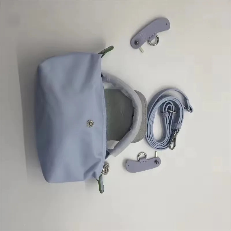 A light blue waterproof nylon crossbody bag with a detachable mini pouch and strap accessories hanging on a white wall.