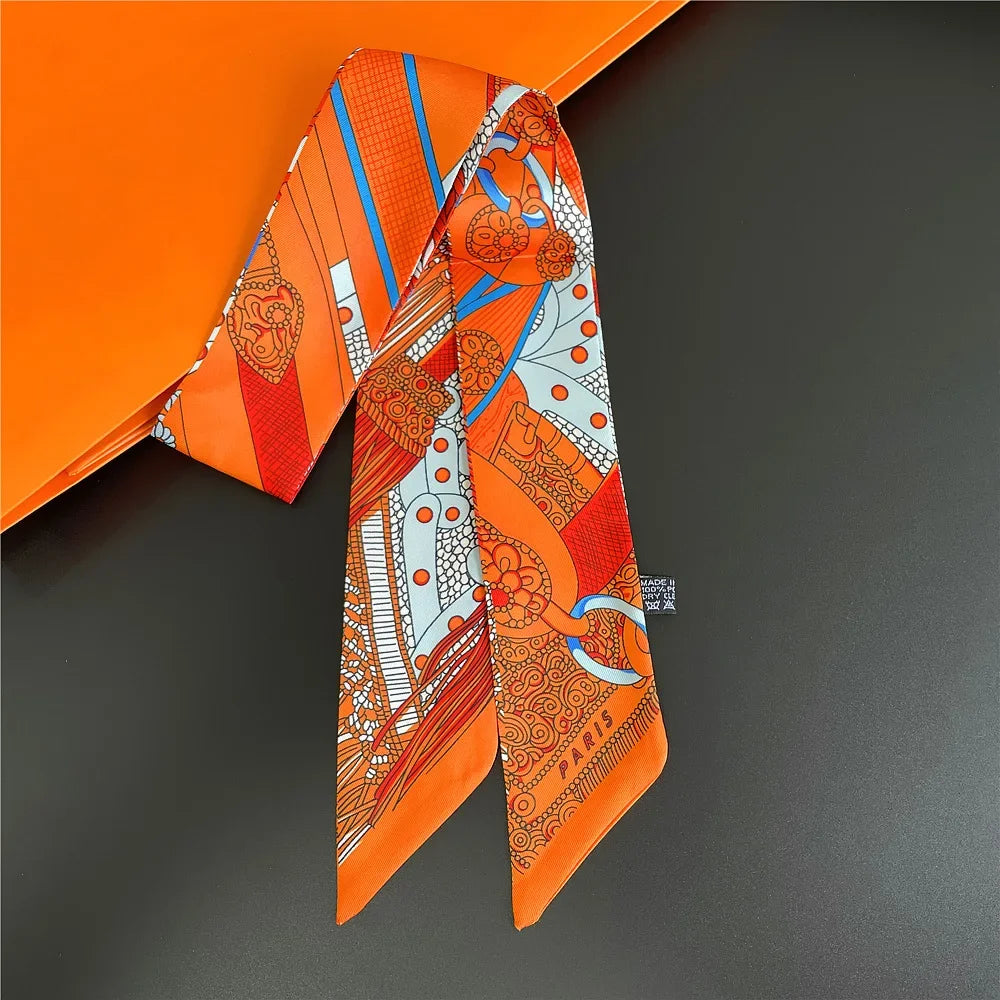 Orange silk twill ribbon scarf with intricate orange and white patterns displayed on a dark surface.