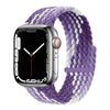 A silver Apple Watch is shown with a purple and white braided stretch band wrapped around it.
