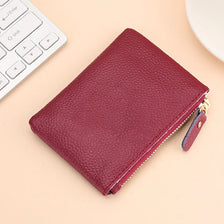 A deep burgundy genuine leather mini zipper coin and card purse resting on a light beige surface next to a white keyboard.