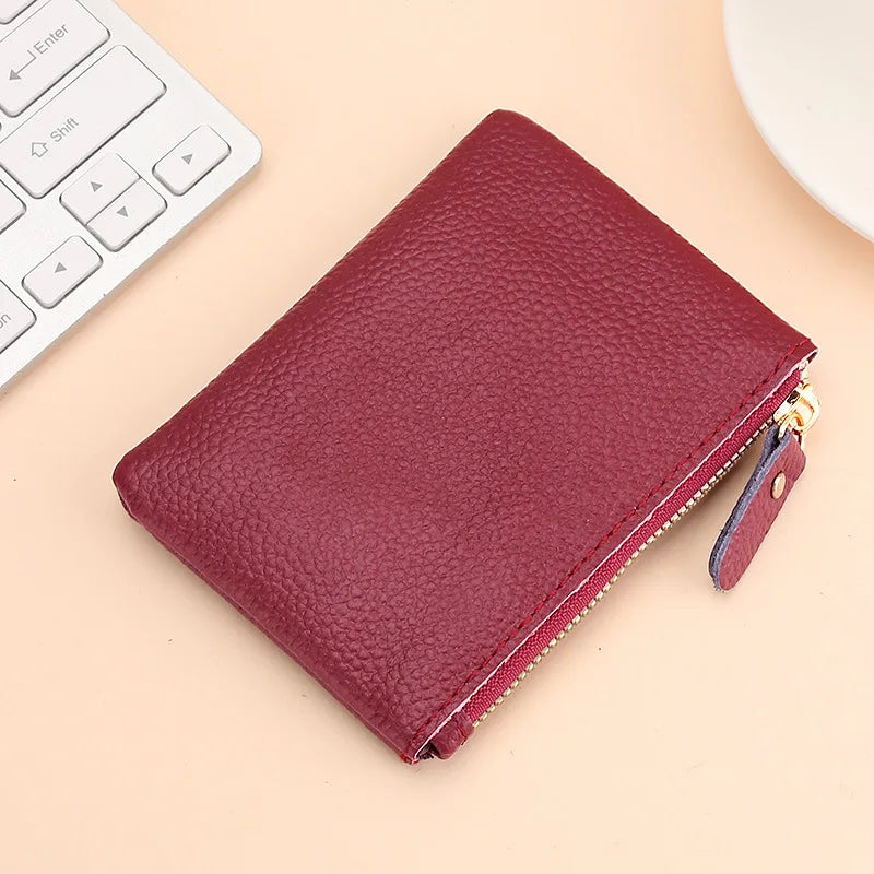 A deep burgundy genuine leather mini zipper coin and card purse resting on a light beige surface next to a white keyboard.