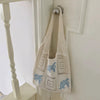 A cream-colored knitted tote bag with blue floral embroidery hanging on a white door frame.