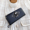 A black leather wallet with silver skull and floral design resting on a cream textured fabric.