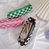A set of three checkered makeup bags in green, pink, and black patterns lying on a white surface.