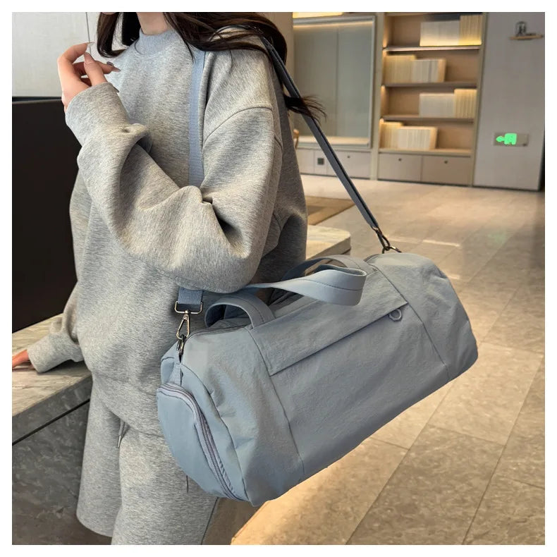 A person is holding a light gray Oxford gym duffel bag with a blue strap in an indoor setting.