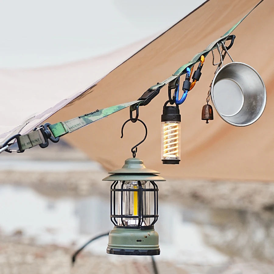 A durable outdoor camping crossbody strap with attached lights and a metal bowl is suspended from a tent fabric.