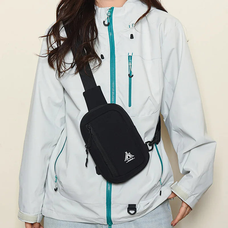 A person is wearing a light gray jacket with a black sling crossbody bag attached to the front zipper.