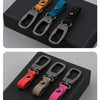 Three leather keyring keychains in brown, blue, and black are displayed on a dark surface.