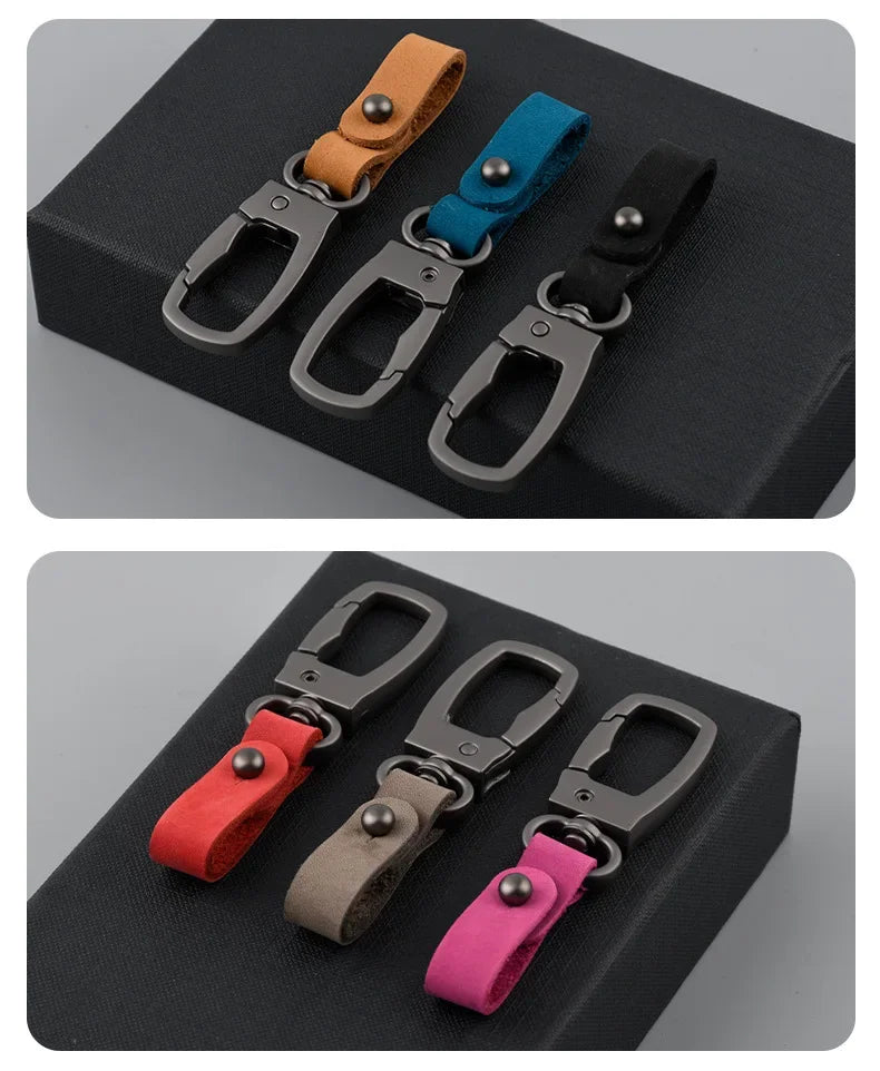Three leather keyring keychains in brown, blue, and black are displayed on a dark surface.