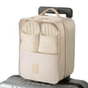 A beige portable luggage shoe organizer bag with a handle resting on a silver suitcase.