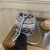 A navy and cream patterned drawstring bucket bag with light blue straps resting on a glass surface.