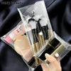 A transparent portable organizer pouch containing makeup brushes, a powder compact, and cosmetic tools.