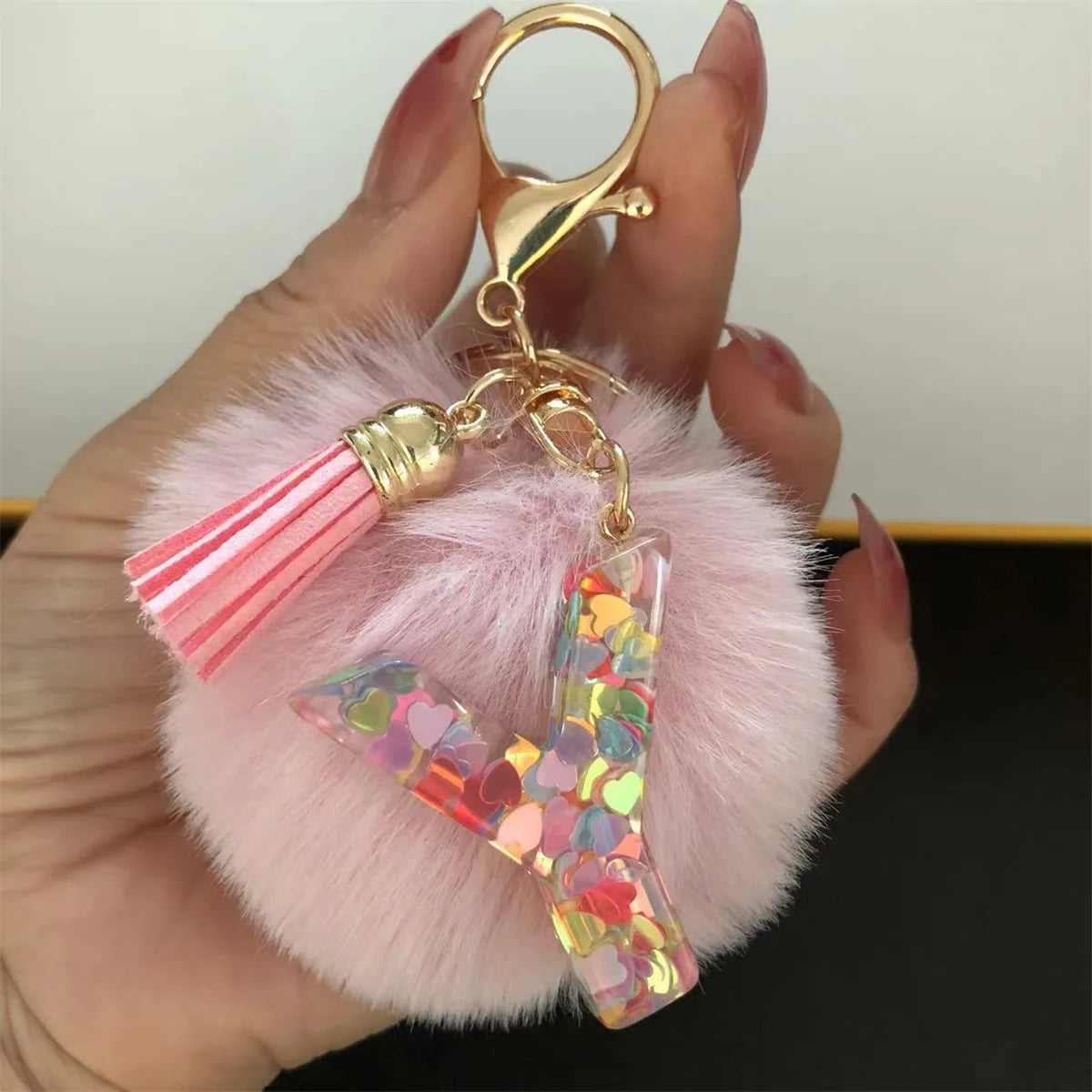 A hand holds a custom initial letter keychain featuring a shiny resin pendant and pink alphabet charm.