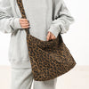 A person wearing a gray sweatshirt holds a brown leopard print canvas shoulder bag with an adjustable strap.