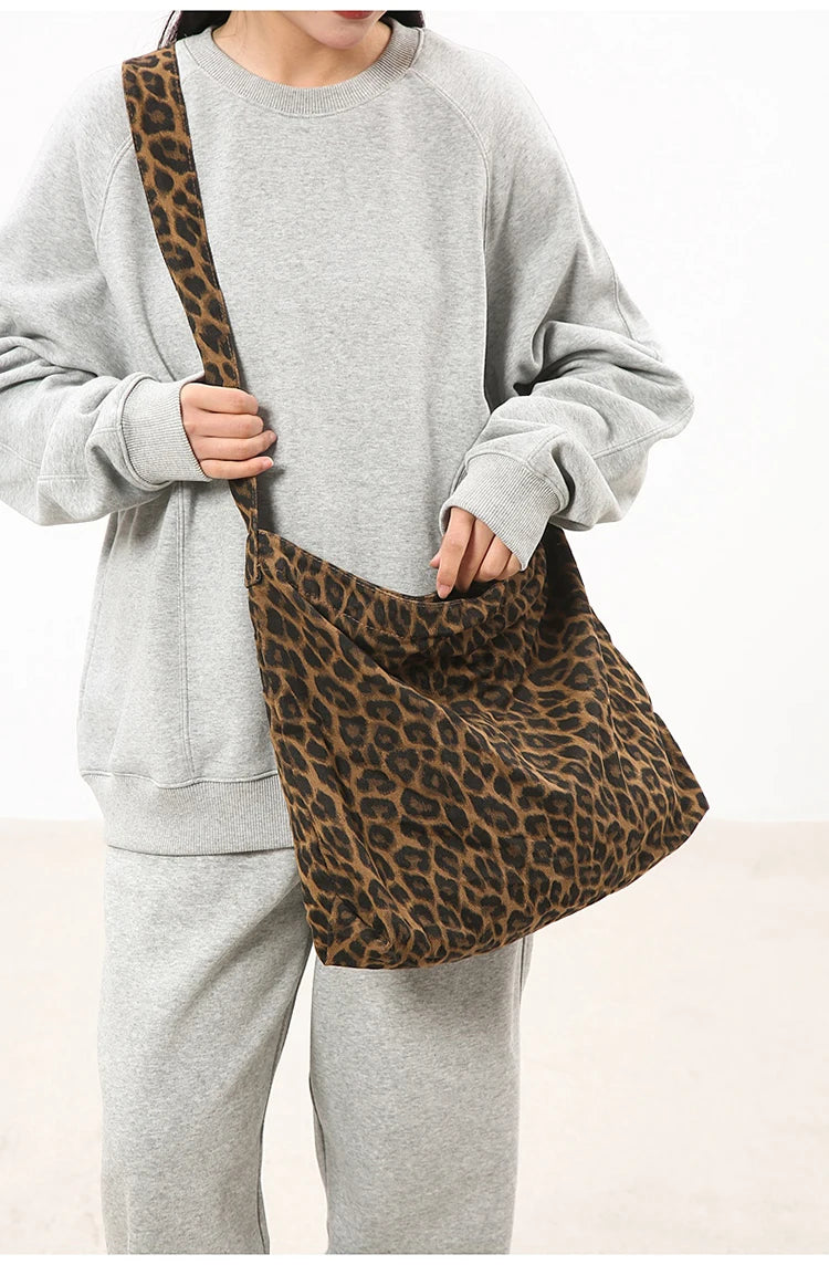 A person wearing a gray sweatshirt holds a brown leopard print canvas shoulder bag with an adjustable strap.