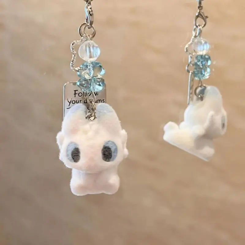 A silver keychain pendant featuring a white cartoon character resembling Toothless, with blue gemstone accents.