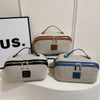A beige travel toiletry bag with brown leather accents and a blue version, displayed next to a framed sign.