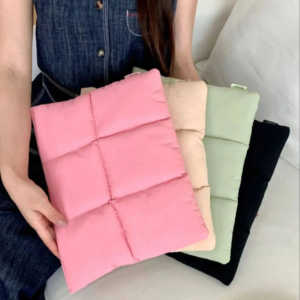 A stack of pink, beige, and green quilted laptop sleeves is held by a person.