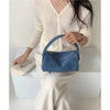 A woman wearing a cream knit sweater holds a navy blue faux suede crossbody bag.