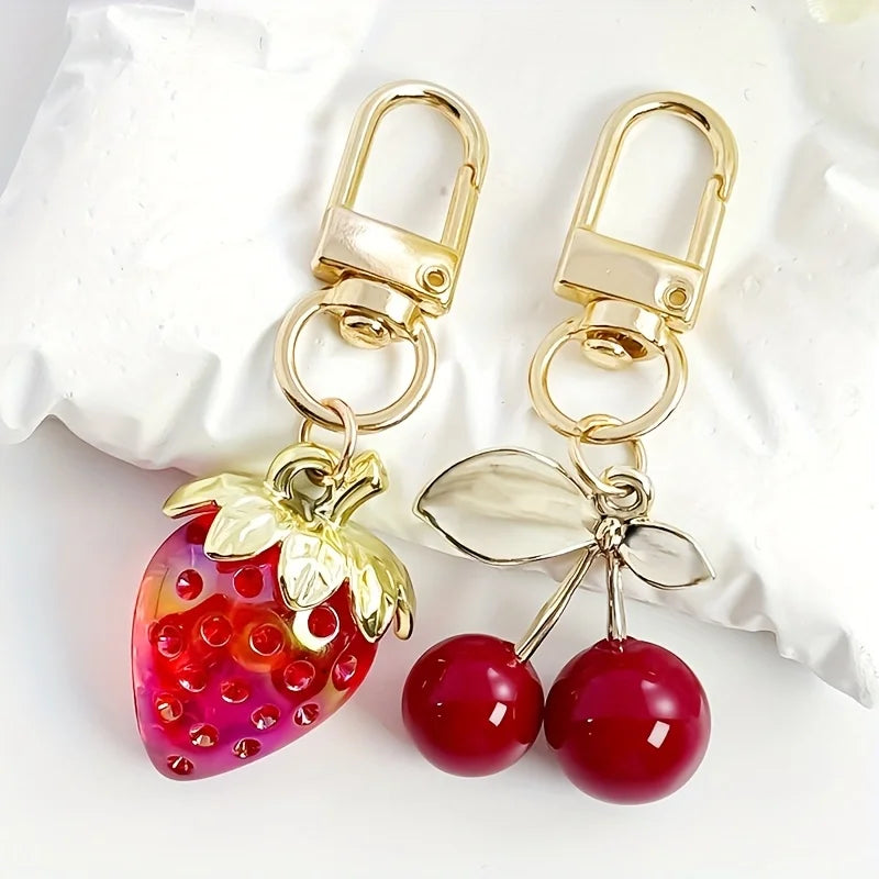 A set of gold-toned keychain charms featuring a strawberry and cherry fruit design.