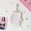 A clear display case framed in pink and green, featuring angel wings, suspended from a silver star charm.