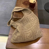 A beige knitted shoulder bag with a mesh pattern resting on a wooden table.