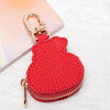 Cartera de monedas con forma de panda roja y texturizada, con cierre y cadena dorada sobre fondo rosa claro.