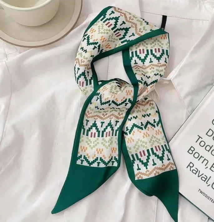 Écharpe de soie vert foncé et crème à motif, nouée en nœud, portée sur un chemisier blanc.
