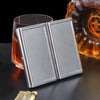 A pair of silver metal cigarette holders resting on a dark surface next to an amber glass.