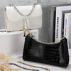 A black crocodile-skin leather handbag with a gold chain strap displayed next to a white quilted leather purse.