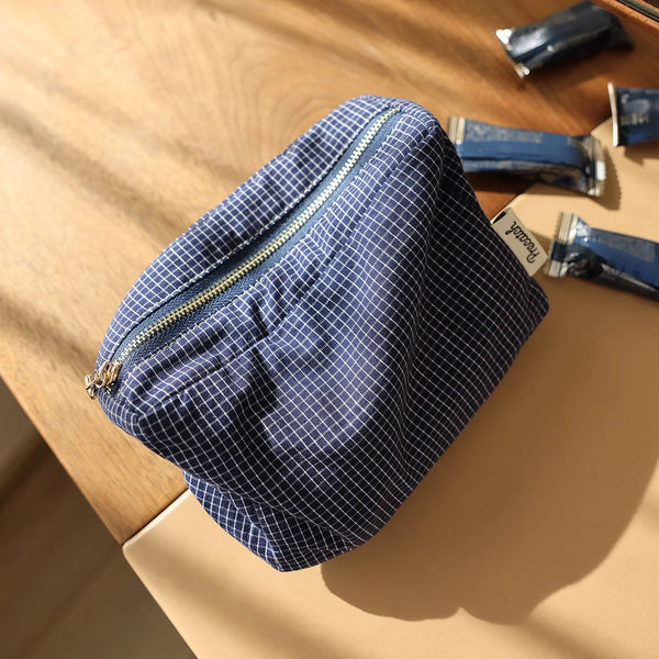 A navy blue and white checkered fabric cosmetic storage pouch resting on a light wooden surface.