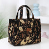 A black and tan patterned cloth tote bag with handles is displayed on a white surface.