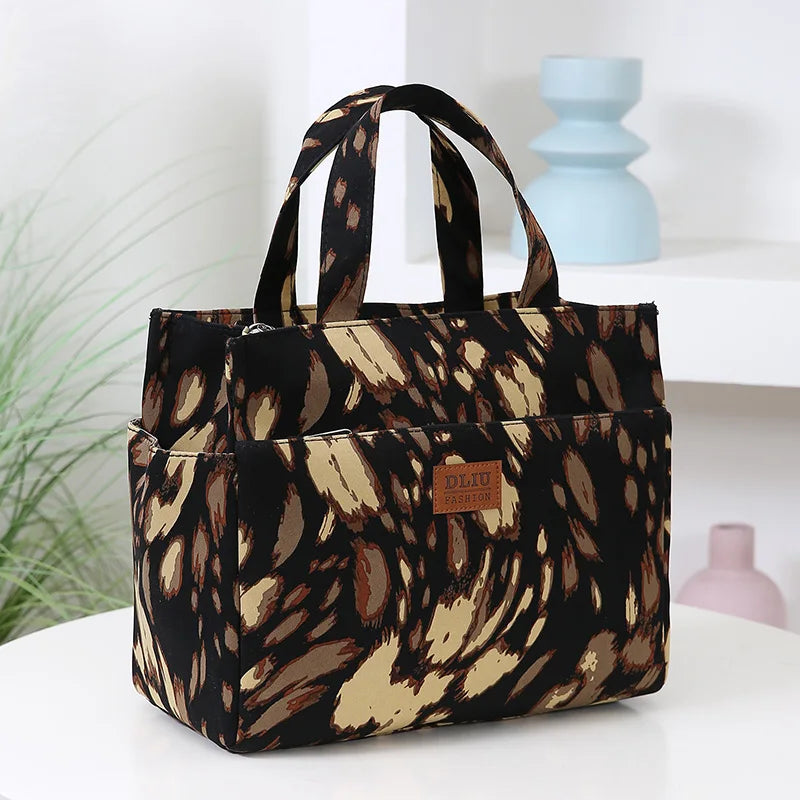 A black and tan patterned cloth tote bag with handles is displayed on a white surface.