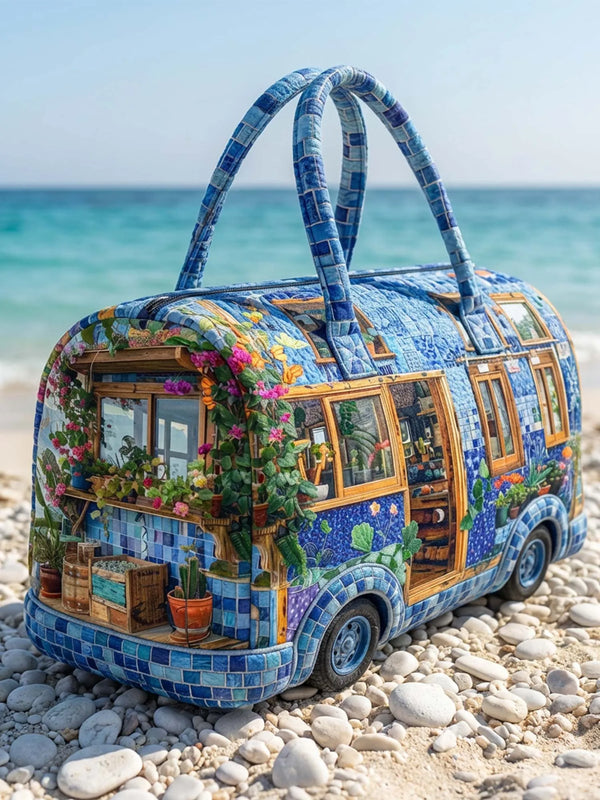 A colorful, tiled travel tote bag shaped like a vintage suitcase with handles, resting on light-colored pebbles.