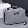 A gray portable waterproof travel toiletry bag resting on a light-colored surface next to a white sink.
