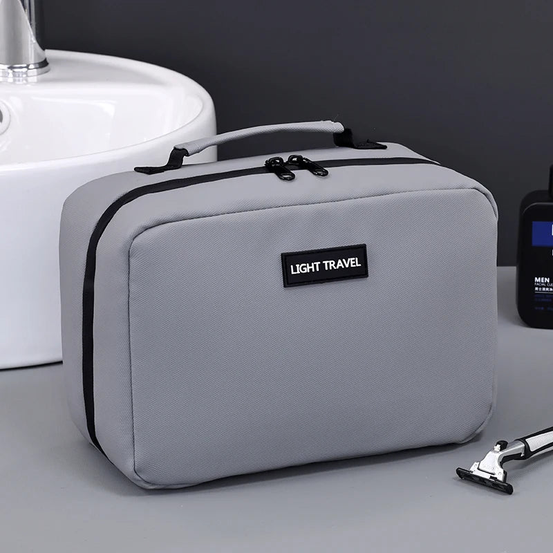 A gray portable waterproof travel toiletry bag resting on a light-colored surface next to a white sink.
