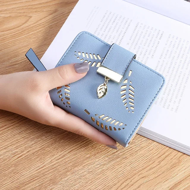 Una mano sostiene un bolso de mano de cuero PU azul claro con detalles dorados sobre una superficie de madera.