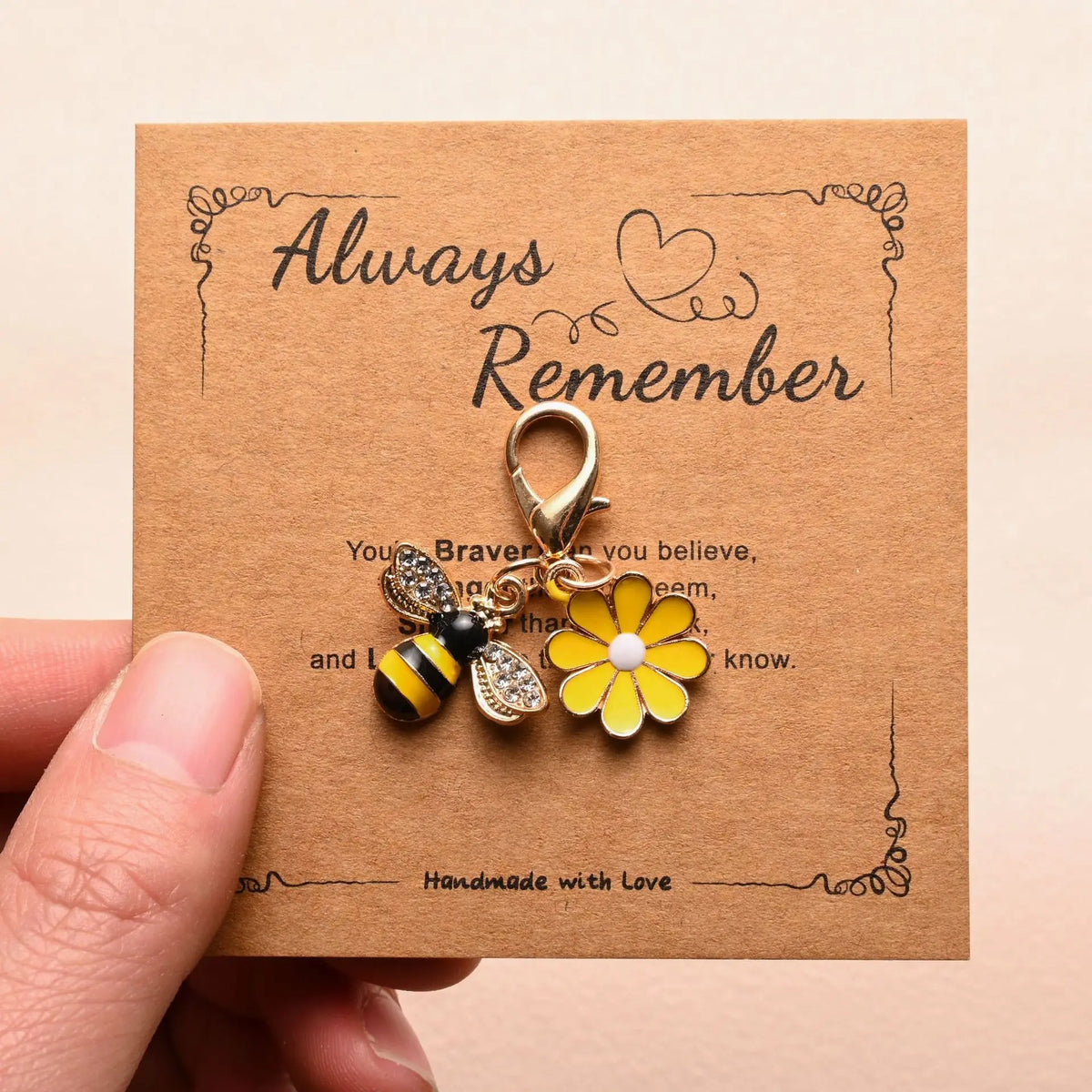 A gold-colored charm featuring a yellow flower and a black and yellow bee, presented on a kraft paper card.
