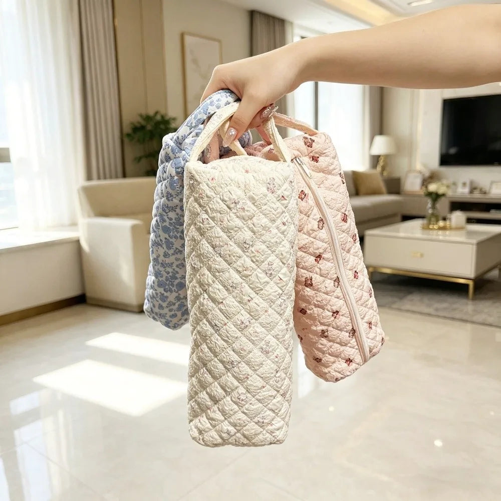 A hand is holding a quilted storage bag for hair dryer and personal items with various fabric patterns.