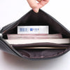 A hand is opening a dark brown PU leather clutch bag to reveal stacked papers inside.